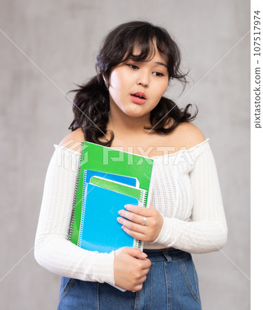 Pensive young girl with notebooks posing in studio 107517974