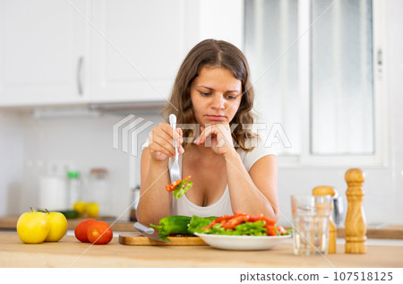 Portrait of displeased woman eating salad at home Portrait of displeased woman eating salad at home 107518125