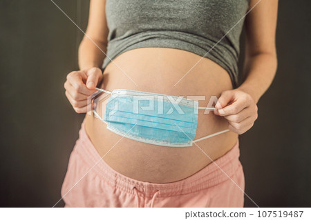 Belly of a pregnant woman holding medical mask close up Belly of a pregnant woman holding medical mask close up 107519487