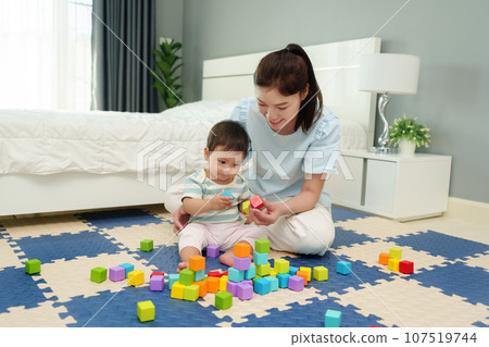 happy infant baby playing wooden block toy with mother on jigsaw mat in bedroom 107519744