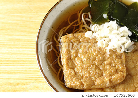 An overhead shot of fox soba noodles topped with two pieces of fried tofu, seaweed, and green onions. 107523606