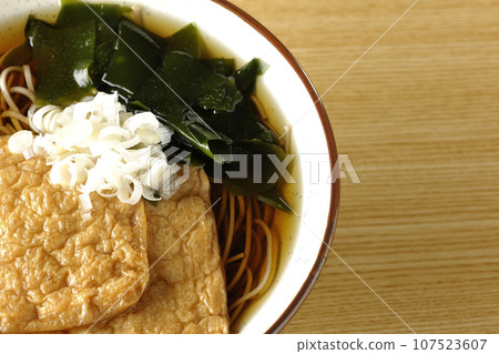 An overhead shot of fox soba noodles topped with two pieces of fried tofu, seaweed, and green onions. An overhead shot of fox soba noodles topped with two pieces of fried tofu, seaweed, and green onions. 107523607