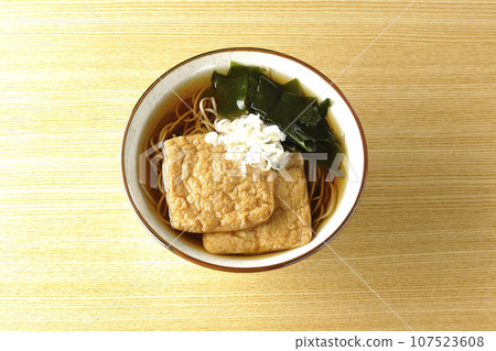 An overhead shot of fox soba noodles topped with two pieces of fried tofu, seaweed, and green onions. 107523608