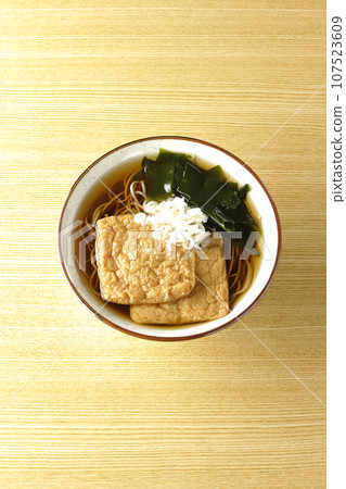 An overhead shot of fox soba noodles topped with two pieces of fried tofu, seaweed, and green onions. 107523609