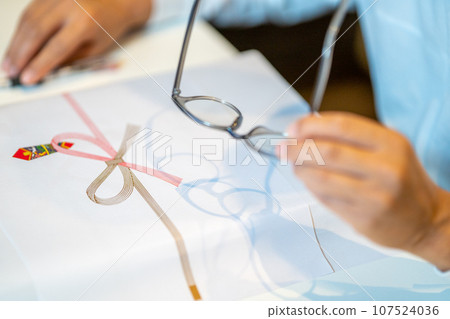 A person wearing reading glasses and preparing a postcard as a return gift. A person wearing reading glasses and preparing a postcard as a return gift. 107524036