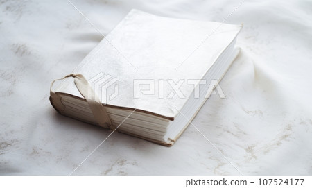 a white book with a ribbon on a white marble surface. The book has a textured cover and the ribbon is tied in a bow. The marble background has gray veins and adds elegance to the image a white book with a ribbon on a white marble surface. The book has a textured cover and the ribbon is tied in a bow. The marble background has gray veins and adds elegance to the image 107524177