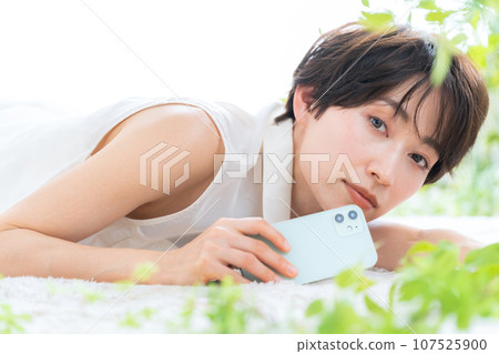 Middle-aged woman lying in the living room looking at her smartphone 107525900