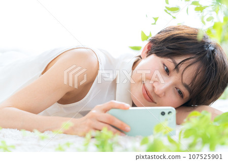 Middle-aged woman lying in the living room looking at her smartphone Middle-aged woman lying in the living room looking at her smartphone 107525901