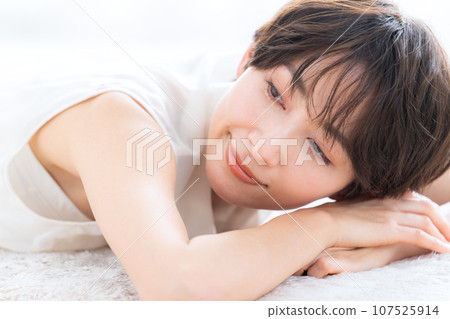 A middle-aged woman lying down in the living room and doing skin care 107525914