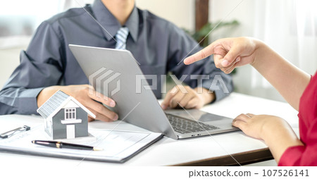 A real estate agent with a House model is talking to clients about buying home insurance. Home insurance concept A real estate agent with a House model is talking to clients about buying home insurance. Home insurance concept 107526141