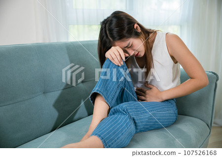 Asian young woman unhappy closing eyes with stomach ache on sofa in living room, female pain lying on couch at home, suffering from strong abdominal painful colon problem feeling unwell Asian young woman unhappy closing eyes with stomach ache on sofa in living room, female pain lying on couch at home, suffering from strong abdominal painful colon problem feeling unwell 107526168