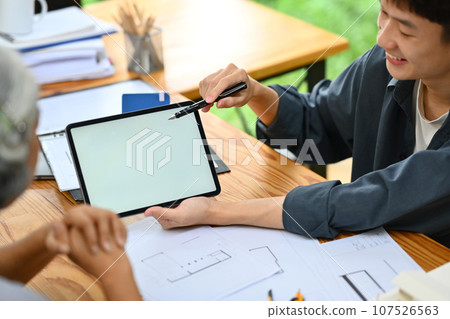 Smiling architect man pointing at digital tablet screen, explaining house renovation plan to client Smiling architect man pointing at digital tablet screen, explaining house renovation plan to client 107526563