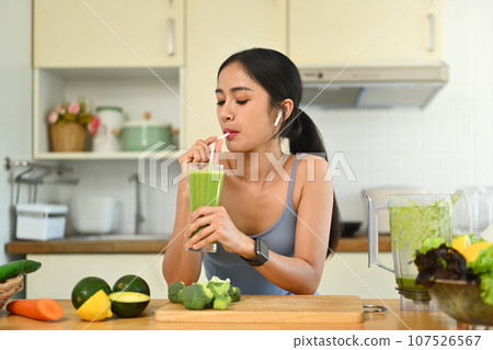 Beautiful young woman in sportswear drinking green vegetables smoothie after her morning workout 107526567