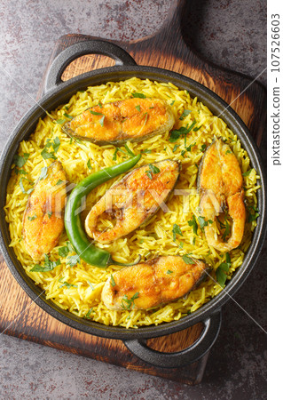 Ilish Polao or Hilsa Pulao is a Asian spicy Fish Pilaf closeup on the black pan on the table. Vertical top view 107526603