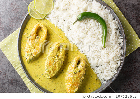 Portion of the popular Hilsa or Ilish fish stewed in mustard sauce with a side dish of white rice close-up in a plate. horizontal top view 107526612