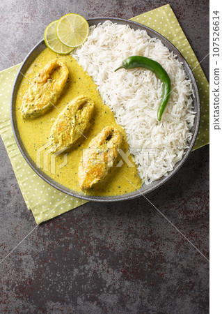 Illish or Hilsa fish cooking with mustard seed sauce served with white rice closeup on the plate. Vertical top view Illish or Hilsa fish cooking with mustard seed sauce served with white rice closeup on the plate. Vertical top view 107526614