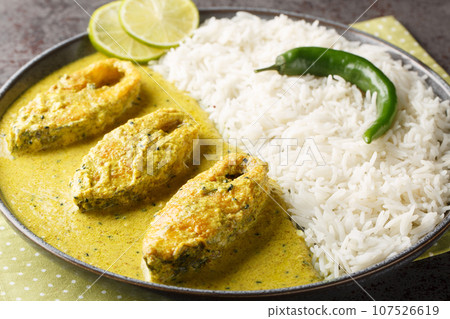 Portion of the popular Hilsa or Ilish fish stewed in mustard sauce with a side dish of white rice close-up in a plate. horizontal 107526619