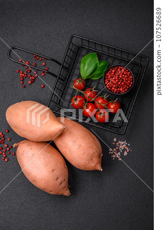 Fresh large pink sweet potato tubers with tomatoes and spices on a dark background 107526689