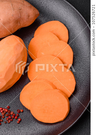 Fresh large pink sweet potato tubers with tomatoes and spices on a dark background Fresh large pink sweet potato tubers with tomatoes and spices on a dark background 107526721
