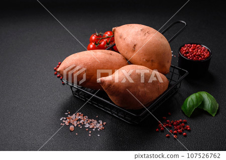 Fresh large pink sweet potato tubers with tomatoes and spices on a dark background Fresh large pink sweet potato tubers with tomatoes and spices on a dark background 107526762