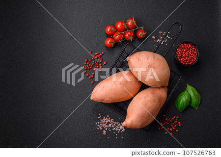 Fresh large pink sweet potato tubers with tomatoes and spices on a dark background Fresh large pink sweet potato tubers with tomatoes and spices on a dark background 107526763