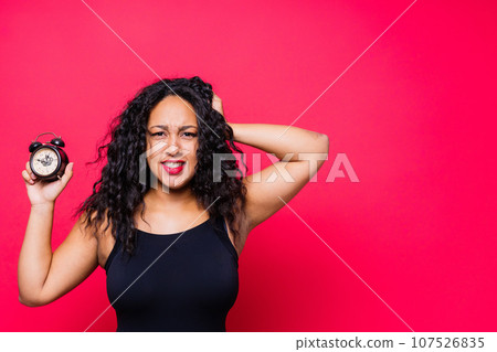 Smiling young african american woman posing isolated on red background with clock 107526835