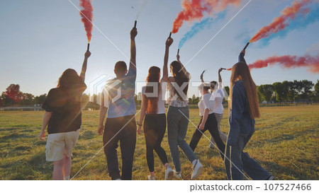 A group of friends spraying multi-colored smoke at sunset. 107527466