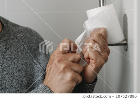 man sitting in the toilet taking a piece of paper 107527890