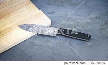 Damascus steel knife on a wooden board 107528497