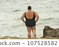 Obese woman in swimsuit standing at beach 107528582