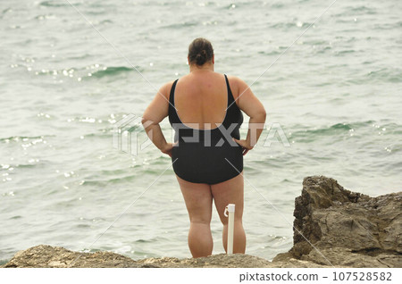 Obese woman in swimsuit standing at beach Obese woman in swimsuit standing at beach 107528582