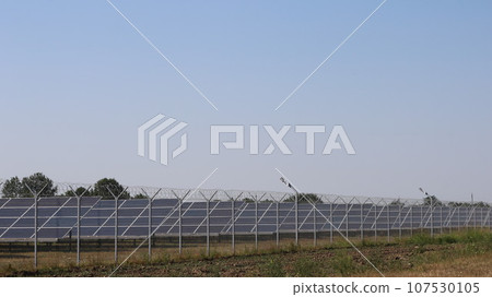 a complex of solar panels standing on a country field behind a wire fence, solar panels in operation, modern equipment used in the field of energy saving and alternative energy a complex of solar panels standing on a country field behind a wire fence, solar panels in operation, modern equipment used in the field of energy saving and alternative energy 107530105