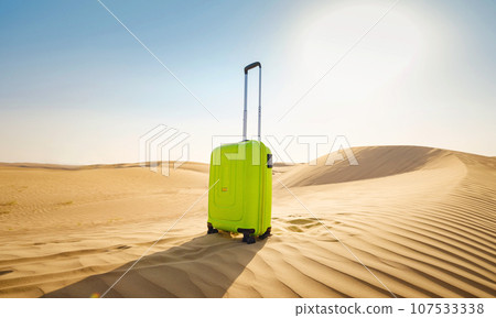 bright light green or yellow suitcase in sands of desert dunes. Concept and idea of travel to United Arab Emirates, Dubai sands at sunset. Summer holiday travel concept bright light green or yellow suitcase in sands of desert dunes. Concept and idea of travel to United Arab Emirates, Dubai sands at sunset. Summer holiday travel concept 107533338