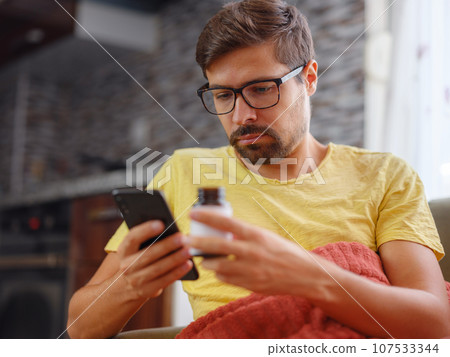 Young Caucasian man using smart phone for reading, searching prescription on bottle medicine, pill label text about information online, instructions side effects, pharmacy medicament concept 107533344