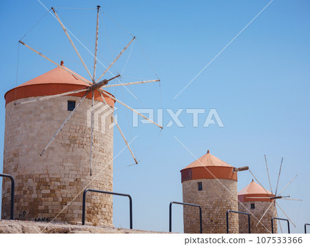 Windmills in the Mandraki port of Rhodes, Greece. Old defensive stands and windmills. Wharf harbors, boats and sailing ships. Historic pier and beach. Travel to Mediterranean islands Rhodes. Windmills in the Mandraki port of Rhodes, Greece. Old defensive stands and windmills. Wharf harbors, boats and sailing ships. Historic pier and beach. Travel to Mediterranean islands Rhodes. 107533366