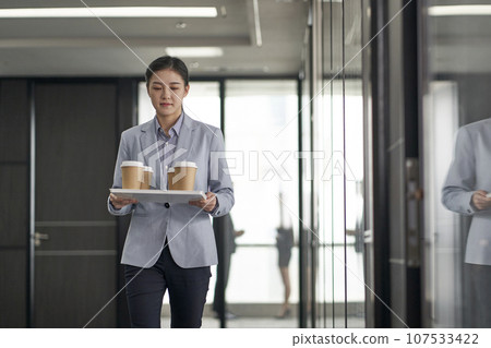 young asian trainee intern carrying a tray of cups of coffee walking in company office young asian trainee intern carrying a tray of cups of coffee walking in company office 107533422