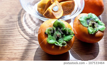 新鮮採摘的柿子和切好的柿子放在玻璃碗裡 107533464