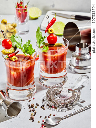 Glasses of bloody mary vodka and tomato juice mix with cocktail utensils on light board. 107533794