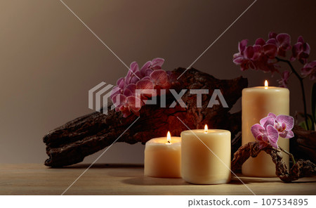 Orchid flowers and burning candles on a background of old wooden snags. Orchid flowers and burning candles on a background of old wooden snags. 107534895