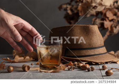 Whiskey with ice on a stone table with dried oak leaves. 107534984