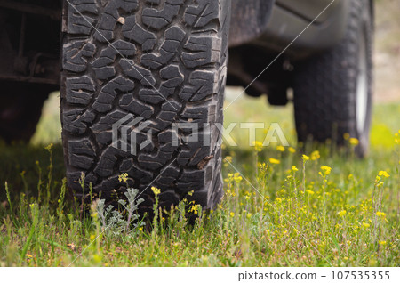 Transport, driving and car concept, close-up of a car wheel on green lush grass. A car wheel stands in the mountains in summer Transport, driving and car concept, close-up of a car wheel on green lush grass. A car wheel stands in the mountains in summer 107535355