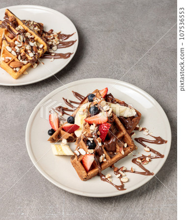 Belgian waffles with chocolate, berries and nuts. Close-up on a gray background. Belgian waffles with chocolate, berries and nuts. Close-up on a gray background. 107536553
