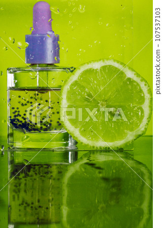 Hyaluronic acid in a glass bottle with a pipette on green background against wet glass and lime slice. Facial Serum or cuticle citrus oil. Hydro boost serum provides active moisturizing for aging skin 107537103