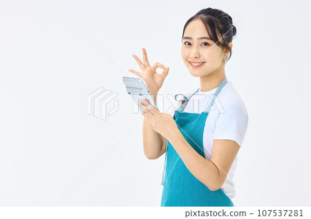 A young housewife wearing an apron using a calculator 107537281