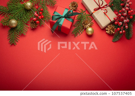 Christmas or New Year celebration red paper festive background with decoration fir tree, wrapped present boxes, cones, berries, sparkly red balls. Space for text. 107537405