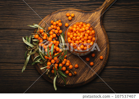 Sea buckthorn ripe berries in glass jar and branches with leaves top view on dark wooden rustic background, great for skin, heart, vessels and immune system. Sea buckthorn ripe berries in glass jar and branches with leaves top view on dark wooden rustic background, great for skin, heart, vessels and immune system. 107537407