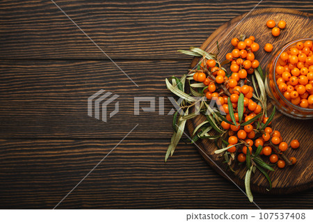 Sea buckthorn ripe berries in glass jar and branches with leaves top view on dark wooden rustic background, great for skin, heart, vessels and immune system. Copy space. Sea buckthorn ripe berries in glass jar and branches with leaves top view on dark wooden rustic background, great for skin, heart, vessels and immune system. Copy space. 107537408