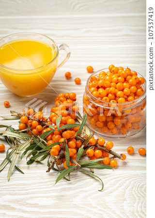 Sea buckthorn healthy hot tea, ripe berries in glass jar and branches with leaves on white wooden rustic background, great for skin, heart, vessels and immune system. 107537419
