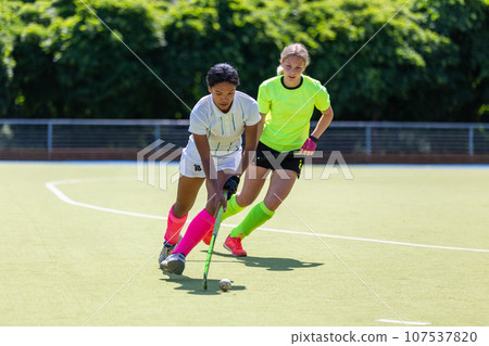 Two female field hockey players fighting for the ball on the pitch in attack 107537820