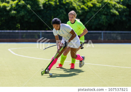 Two female field hockey players fighting for the ball on the pitch in attack 107537821
